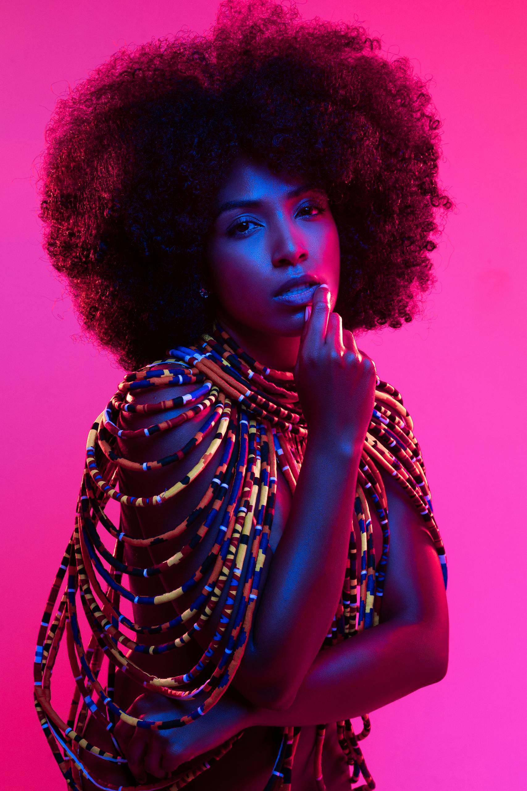 Stylish portrait of a woman with afro hair and beaded fashion in vibrant lighting.