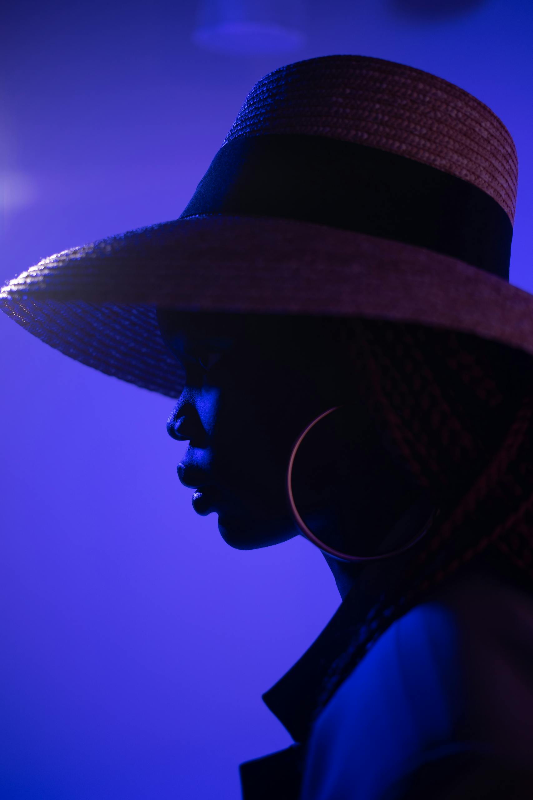 Stylish silhouette of a woman in a fedora hat, highlighted by dramatic blue lighting.