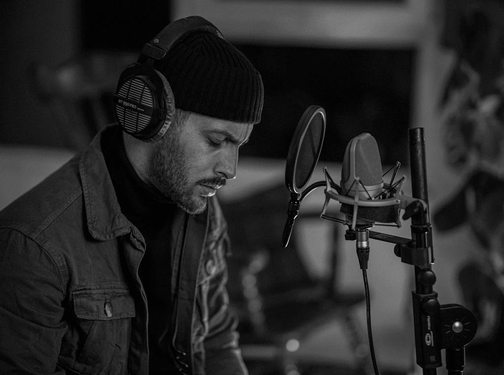 A captivating black and white image of a male musician recording with headphones and a microphone.