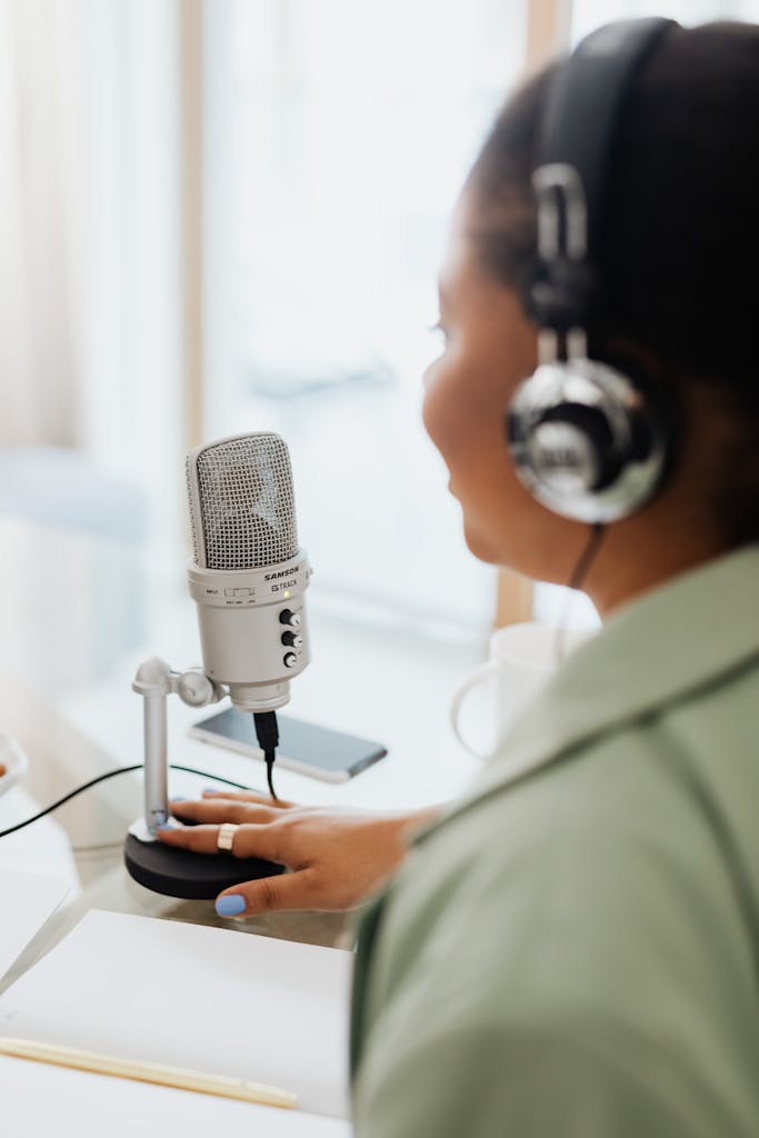 A woman recording a podcast indoors with a microphone and headphones.